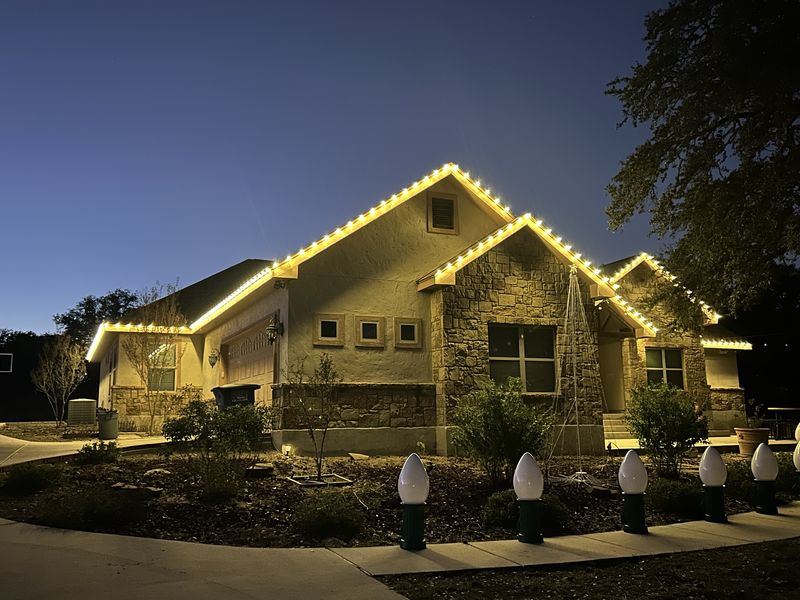 Christmas light installation on a stucco and stone home at dusk, with lit rooflines and gables
