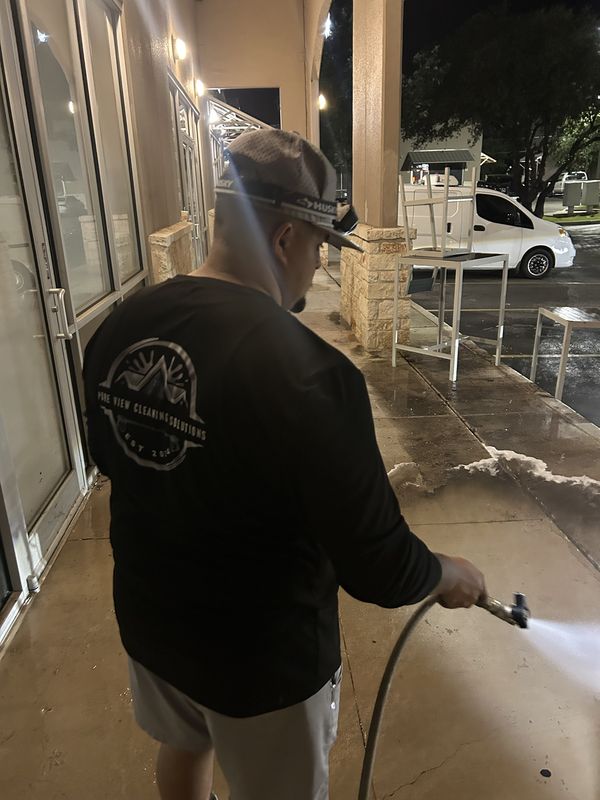 Pure View crew member pressure washing a storefront walkway at night