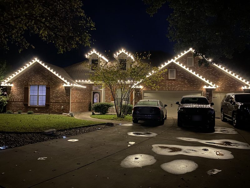 Warm white C9 Christmas lights on the rooflines and dormers of a brick home
