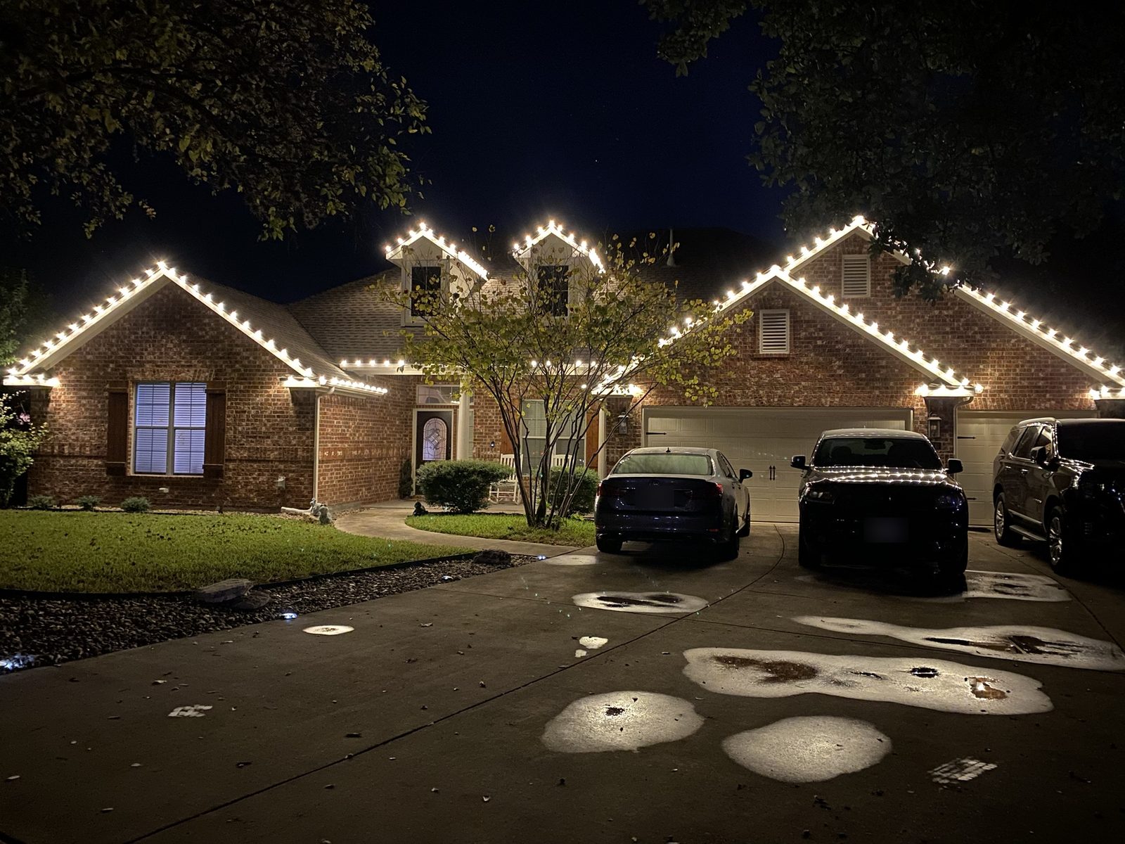 Warm white C9 Christmas lights on the rooflines and dormers of a brick home